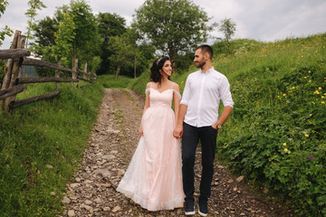 Charming bride hug her handsome groom in mountains. Beautiful wedding couple walk. Green gackground