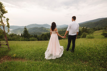 Charming bride hug her handsome groom in mountains. Beautiful wedding couple walk. Green gackground