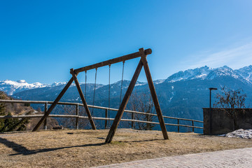 Swing, child's playground with mountain view and snow covered mountains - Italian Alps, Italy