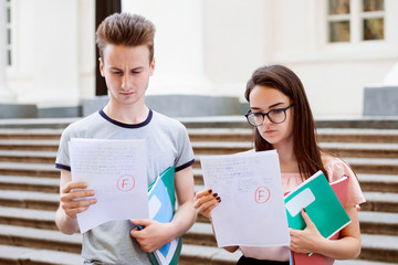 Bewildered and sad students holding papers with bad results of test © Vitalii