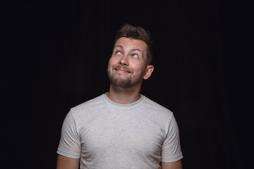 Obraz premium Close up portrait of young man isolated on black studio background. Photoshot of real emotions of male model. Dreaming and smiling, hopeful and happy. Facial expression, human emotions concept.