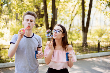 Two friends having fun together blowing soap bubbles in the park