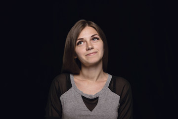 Close up portrait of young woman isolated on black studio background. Photoshot of real emotions of female model. Dreaming and smiling, hopeful and happy. Facial expression, human emotions concept.