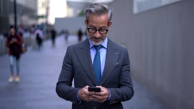 Confident businessman in optical eyewear reading notification on smartphone on way to meeting while received international call via app connected to 4G internet in roaming