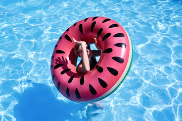 Woman with short hair swimming in a pool, look laughing through pink floatie Inflatable doughnut, blue water. Funny mood.