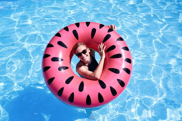 Portrait of woman with short hair swimming in a pool, look laughing through pink floatie Inflatable doughnut, blue water. Funny mood.