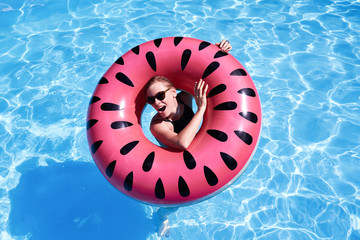 Woman with short hair swimming in a pool, look laughing through pink floatie Inflatable doughnut, blue water. Funny mood. Space for text layout.