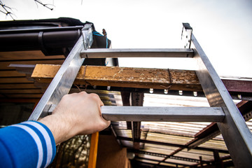 Climbing the ladder. He holds the rung of the ladder with his hand, climbing the roof of the gazebo, home. Checking the condition of the roof, renovation. © Sebastian