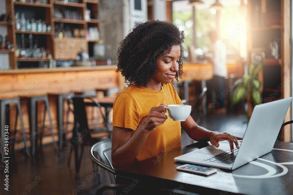 Canvas Prints Young woman holding cup in in hand using laptop