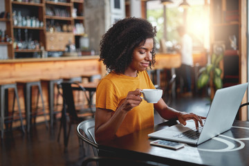 Young woman holding cup in in hand using laptop