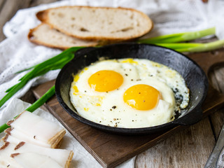 Scrambled eggs in frying pan with pork lard, bread and green feathers onions on old wooden table. National Ukrainian or belorussian food. Breakfast, lunch. Close up, selective focus, rustic style.