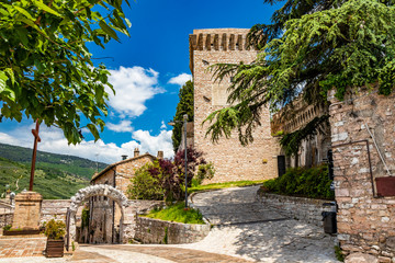 The tower and the medieval walls, in stone and brick, with merlon. A Roman stone arch. In Spello, province of Perugia, Umbria, Italy.