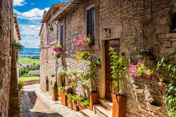 A characteristic alley of the medieval village, with stone and brick houses, plants and flowers on the windows. In Spello, province of Perugia, Umbria, Italy.