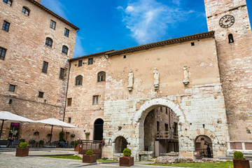 Naklejka premium The Roman consular door, with the tower and the clock. One of the accesses to the city walls. Three statues above the arch. In Spello, province of Perugia, Umbria, Italy.