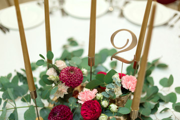 The wedding table setting is decorated with fresh flowers in a brass bowl and golden candles in brass candlesticks. Wedding floristry. Banquet table for guests. Bouquet with dahlias and eucalyptus