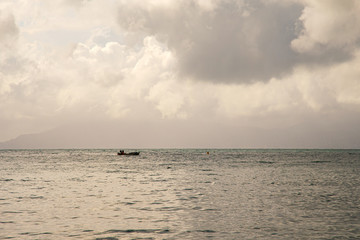 Fototapeta premium Seascape with a fishing boat, a coastline on the foggy horizon in the background and cloudy sky, Sestri Levante, Genoa, Liguria, Italy