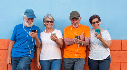 Two couples of senior people standing against an orange and blue wall smiling and looking at the...
