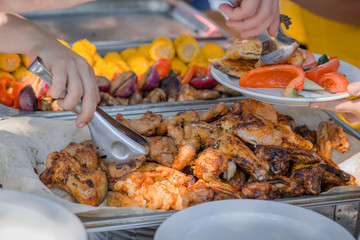 Hand picks the barbecue roasted tasty chicken wings with herbs and sauce from the tray. Outdoors Food.Buffet self-service food/Buffet line with juicy fried chicken wings and vegetables