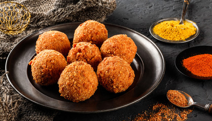Fried potato cheese balls or croquettes with spices on black plate over dark stone background. Unhealthy food, top view