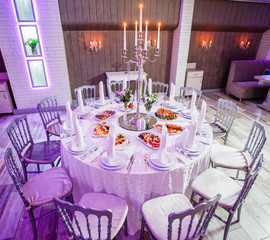 Wedding reception dinner. Round table served with flowers, shiny candles and appetizer food. Holiday banquet menu. Decor of the interior of the banquet hall.