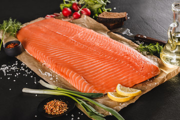Fresh fillet salmon, red fish steak with spices and lemon on craft paper over dark stone...