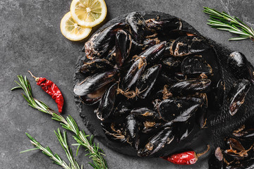 Fresh raw mussels with spices on slate stone over dark background. Seafood, top view, flat lay, copy space