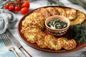 Zucchini fritters are laid out on a plate, in the center there is sour cream sauce with garlic and dill