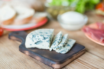Sliced blue cheese on a wooden background and different products. Preparation for cooking snacks.