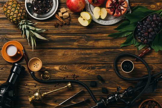 top view of tobacco, hookah, coals, cinnamon, cup of milk and exotic fruits on wooden surface