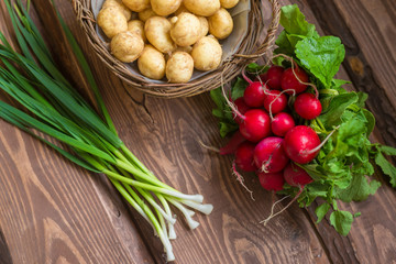 Fresh raw organic vegetables: potatoes, radishes, green onions on a wooden background.