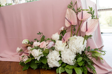 The wedding table setting for the newlyweds is decorated with fresh flowers of carnation, rose, anthurium and eucalyptus leaves. Silver candlesticks, white candles. Wedding floristry. Close-up details