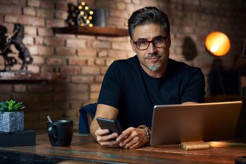 Older man sitting at desk using phone and tablet