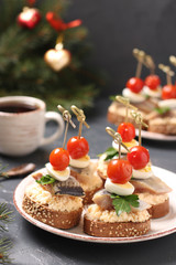 Canapes with salted herring, cheese, quail eggs and cherry tomatoes on rye croutons on the Christmas background