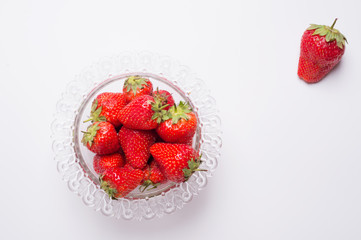 ripe strawberry in glass bowl around white.  flat lay