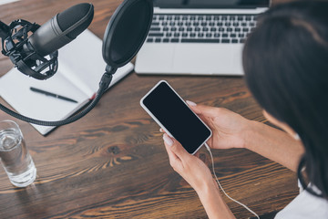 overhead view of radio host holding smartphone with blank screen while sitting at desk near...