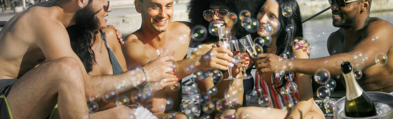 friends drinking champagne at boat party having fun with soap bubbles on foreground.