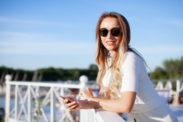 Elegant charming woman texting romantic message on mobile phone. Portrait of luxary lady in glasses enjoying summer sunset in cafe outdoor. Communicating by smartphone in travel..