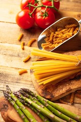 Asparagus, and the artichoke and sprig of tomatoes and sweet red pepper and Italian spaghetti on a cutting board with a knife, sliced. 