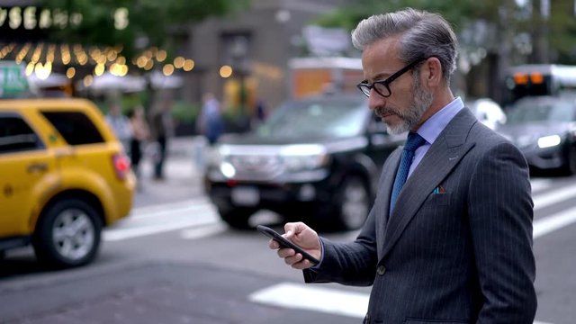 Intelligent man in formal wear holding smartphone and installing application for chatting connected to 4g internet, confident mature male lawyer in eyewear reading text message and sending sms answer