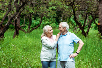 cheerful senior woman looking at husband standing with hand on hip