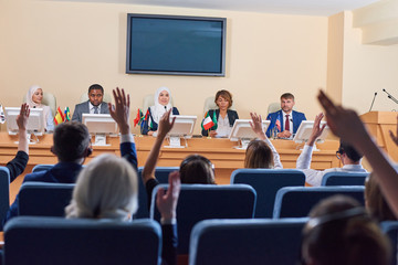 Obraz premium Audience in armchairs raising their hands to ask questions