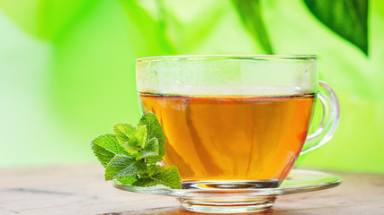 Cup with tea and mint on wooden table.