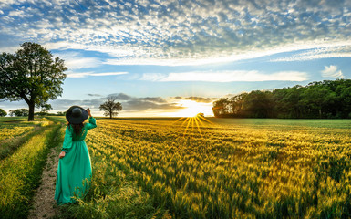 Fototapeta premium Portrait of a beautiful young woman in green dress on meadow watching the sunset enjoying nature