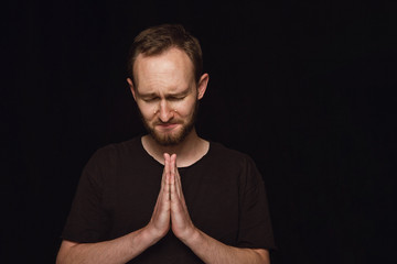 Close up portrait of young man isolated on black studio background. Photoshot of real emotions of male model. Praying with closed eyes and crying. Facial expression, human emotions concept.