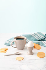 Boiled egg in ceramic egg cup, cup of coffee and thin crispy corn chips on background of turquoise kitchen towel. Breakfast concept. Copy space.