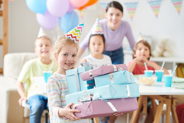 Cute blonde little girl with birthday gifts standing in front of camera