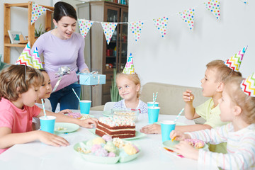 Fototapeta premium Cheerful young woman with birthday gifts standing by table
