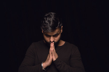 Close up portrait of young man isolated on black studio background. Photoshot of real emotions of male model. Praying looking down, looks hopeful. Facial expression, human emotions concept. © master1305