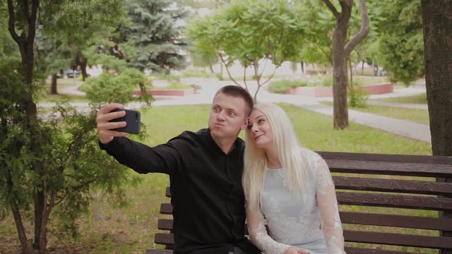 Happy couple in love sitting on a bench in the city park and making selfie on the phone.