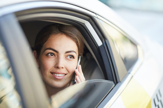 Head and shoulders portrait of beautiful woman speaking by phone in car looking out of window, copy space